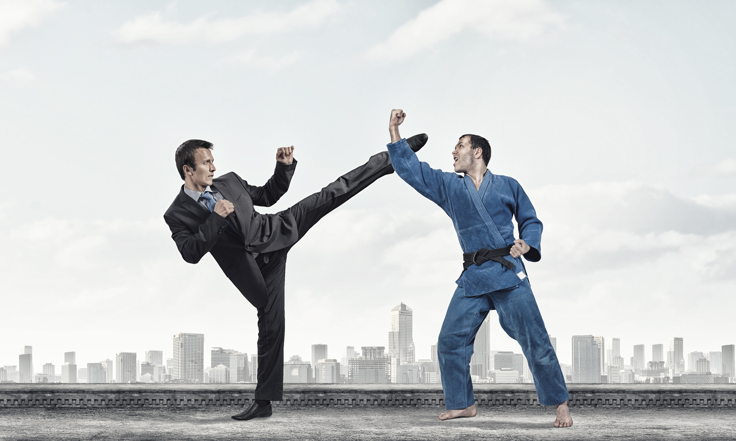 Businessman in suit kicking a martial artist in a blue gi on a rooftop with a cityscape background.