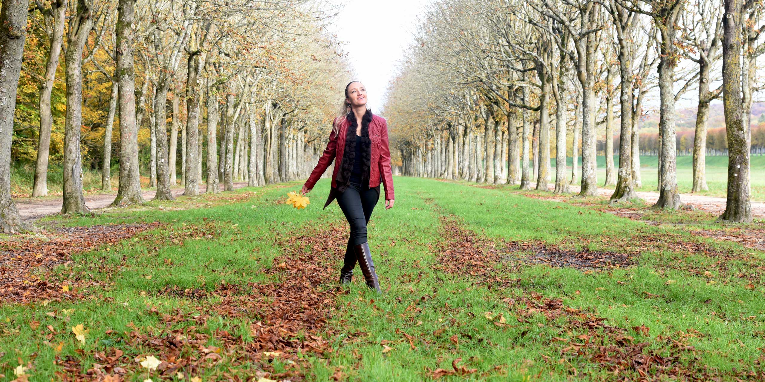 Woman walking in autumn park, holding fall leaves. The park's peaceful setting could inspire meditation.